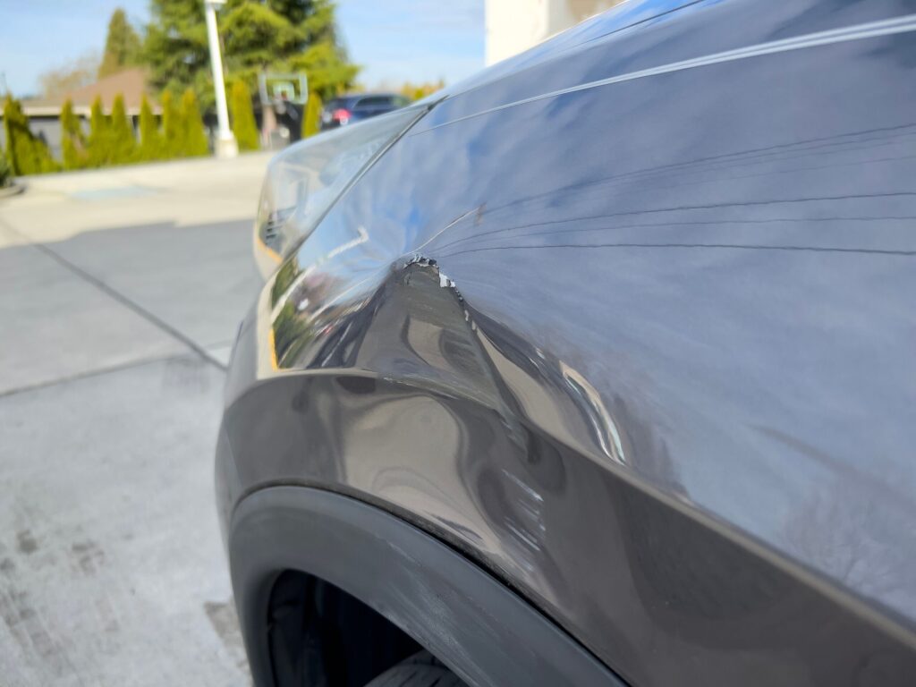 Close up view of a dented and scratched front fender on a grey car.