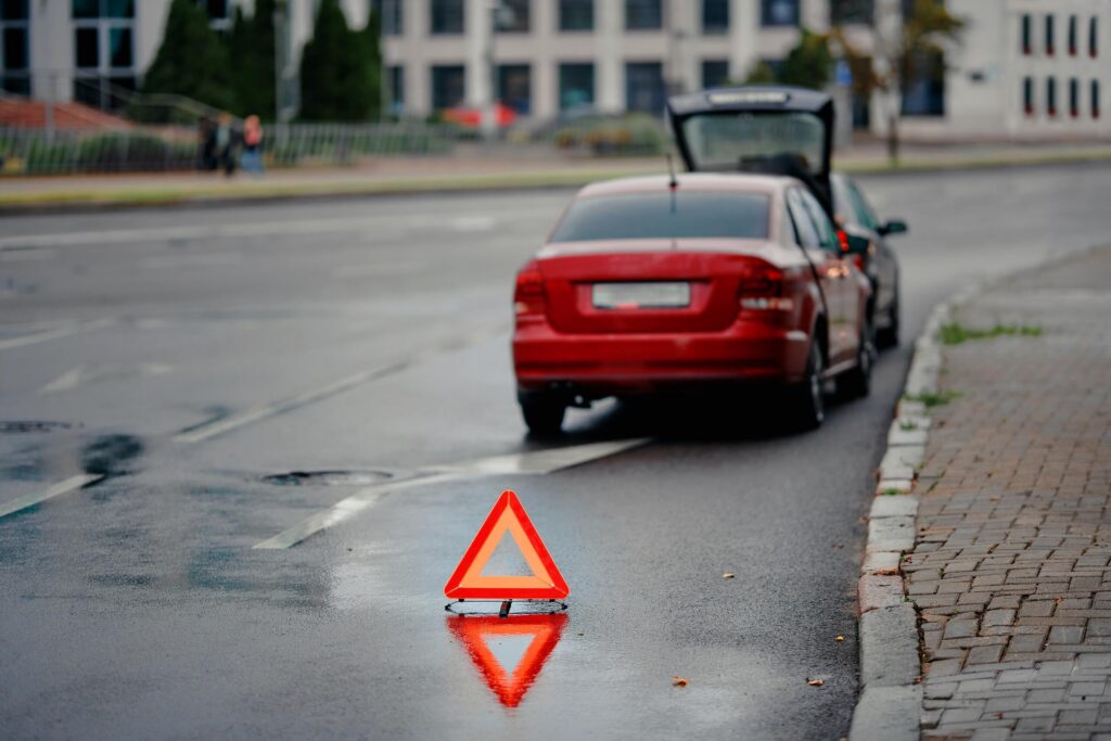 Red emergency reflector triangle standing behind a broken down car on the roadside.