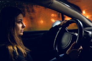 Young woman holding a car driving wheel in a rainy night rain